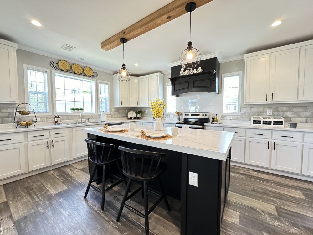 Modern kitchen with white cabinets, a large island with black chairs, pendant lights, and a vase with yellow flowers. Cozy, inviting atmosphere.