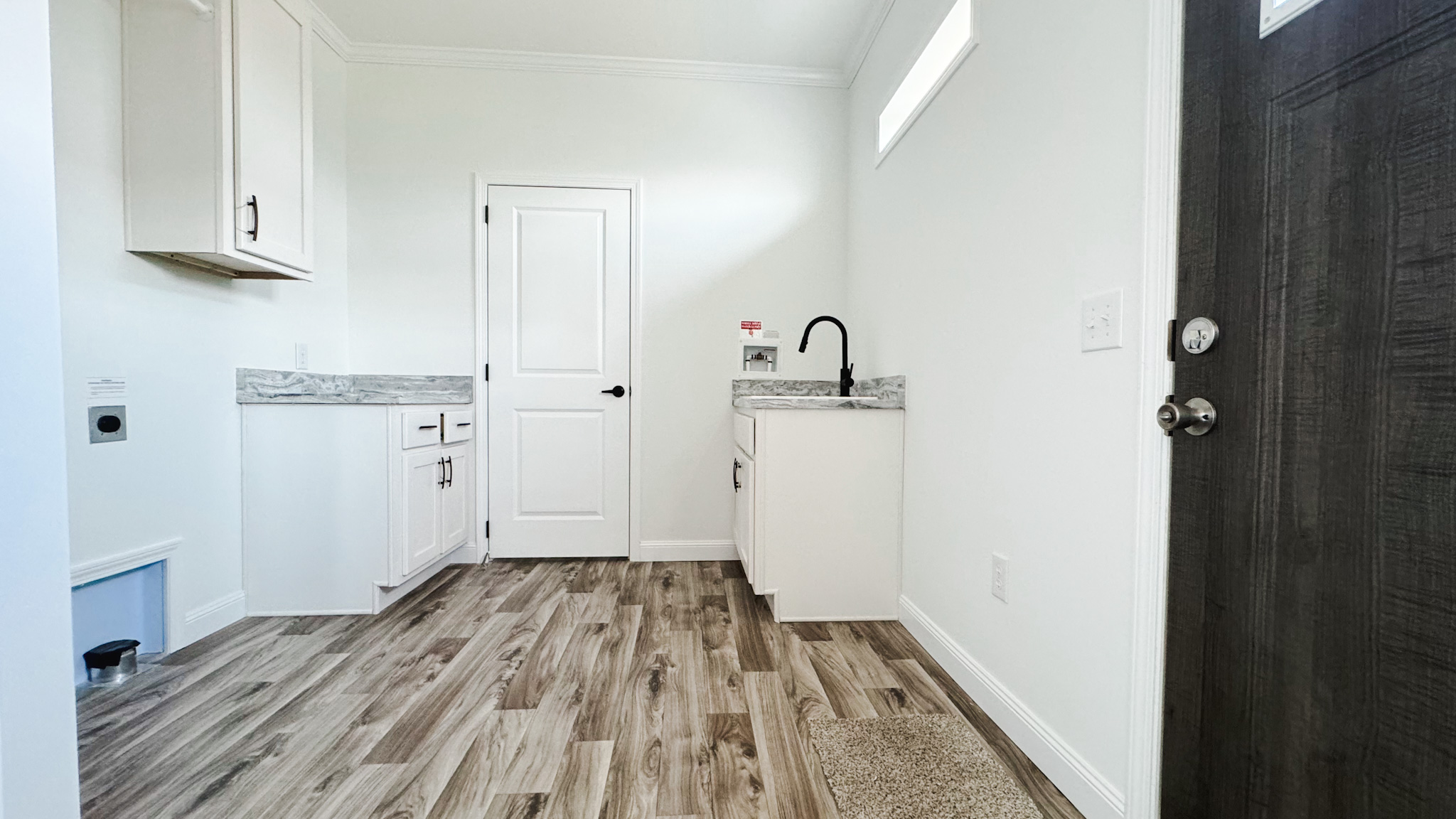 Bright, small laundry room with wood-look flooring, white cabinets, and a marble countertop. Includes a black faucet, white door, and modern decor.