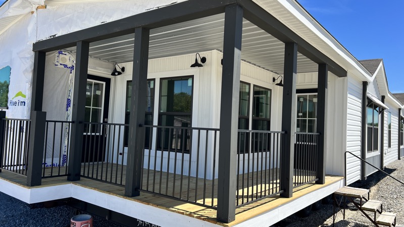 Modern porch with black columns and railings attached to a white house under construction. Bright daylight and clear blue sky enhance the scene.