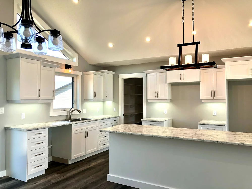 Modern kitchen with white cabinets, marble countertops, and dark wood flooring. Pendant and recessed lighting create a bright, inviting atmosphere.