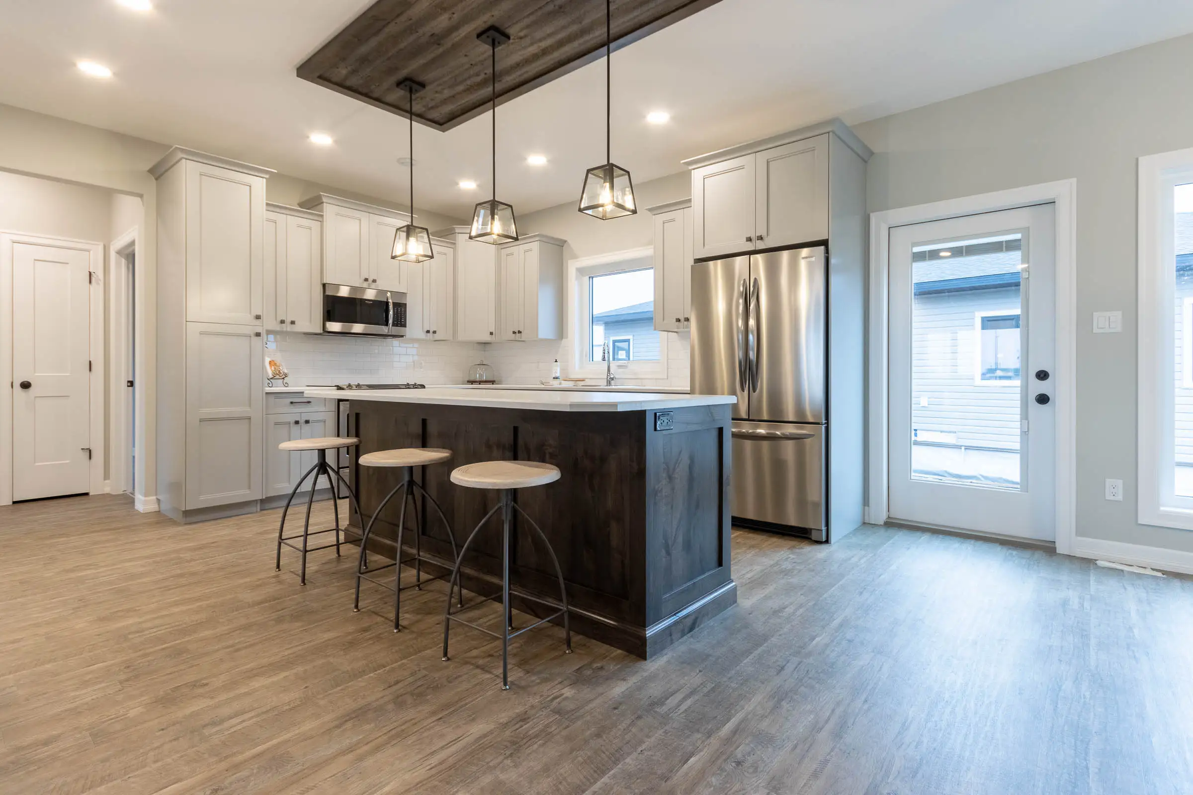 Modern kitchen with light gray cabinets, stainless steel appliances, and a large dark wood island. Three stools and pendant lights create a welcoming tone.