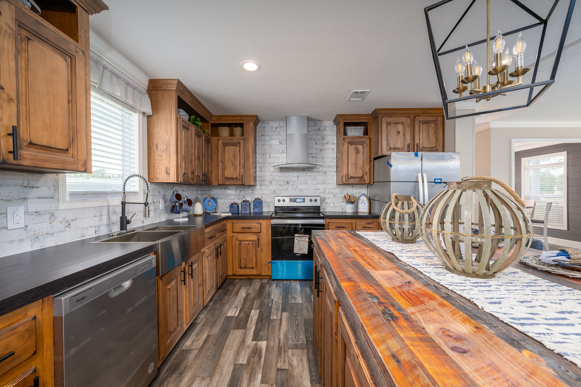 Rustic kitchen with wood cabinets and island, stainless steel appliances, and decorative lanterns. Warm, inviting atmosphere with natural light.