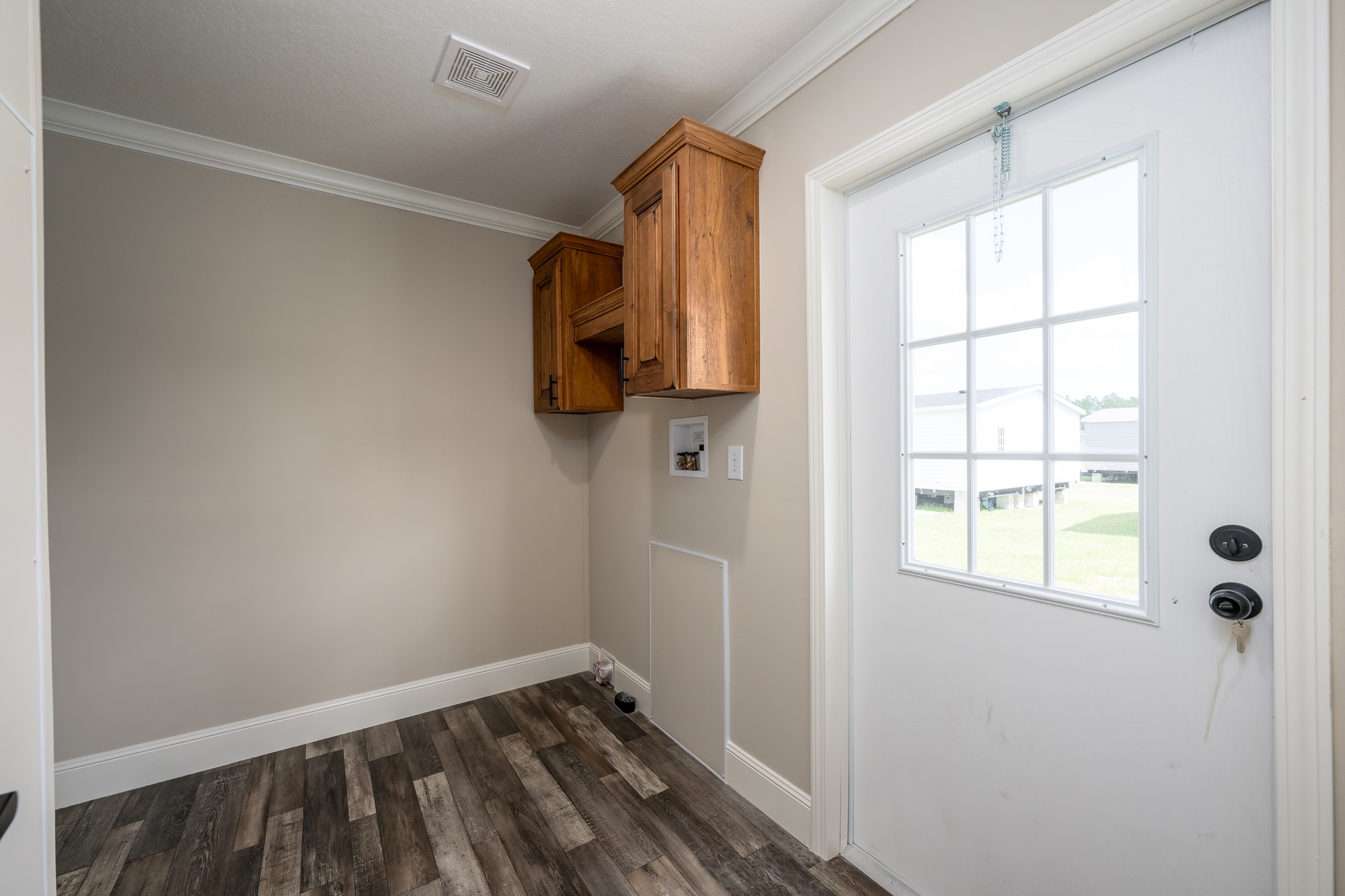 Bright laundry room with light gray walls, dark wood floors, and wooden cabinets. A white door with a grid window leads to the outside.