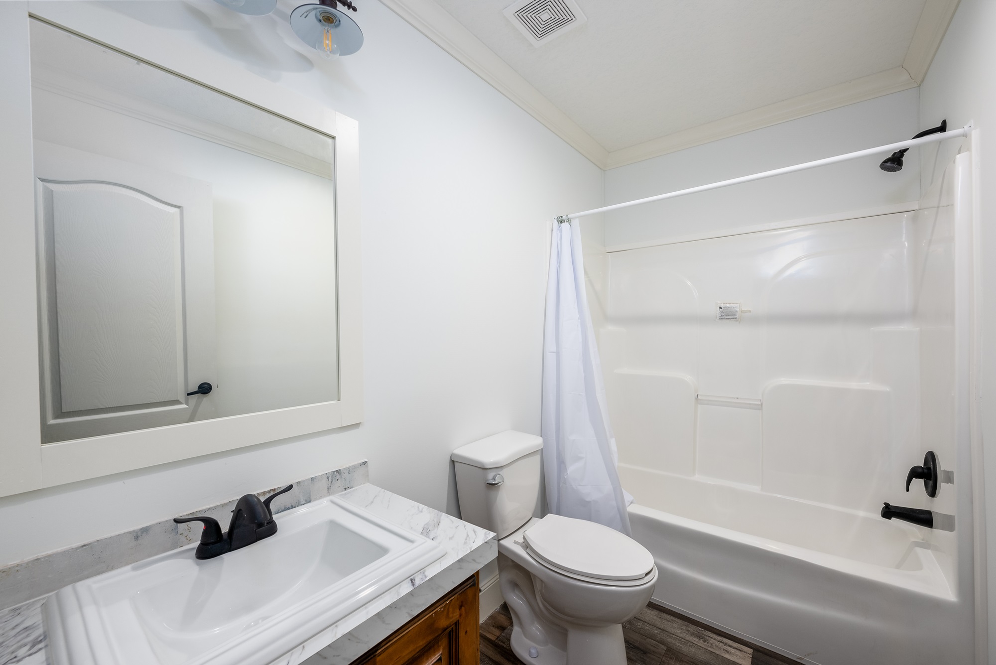 A clean, modern bathroom features a white sink with a marble countertop, a mirror, a toilet, and a bathtub with a shower curtain. The room has a bright, minimalist design.