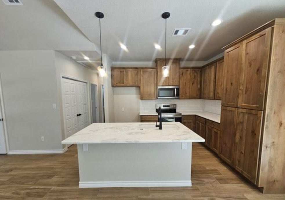 Modern kitchen with a white marble island, wooden cabinets, and stainless steel appliances. Hanging pendant lights create a warm, inviting atmosphere.
