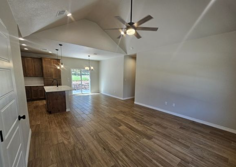 Spacious open-plan living area with wood flooring, ceiling fan, and neutral walls. Kitchen features dark wood cabinets, island, and pendant lights.