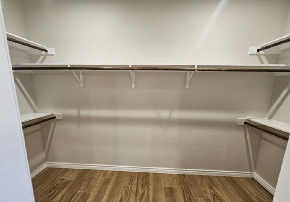 Empty walk-in closet with light wood flooring and white walls. Dark brown shelves line three sides, creating a neat, organized appearance.