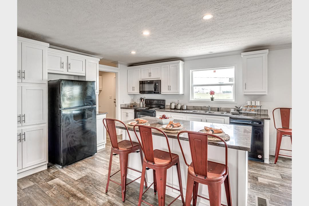 Modern kitchen with white cabinets and stainless steel appliances. A black fridge and stove are present. Four red metal stools line a gray island.