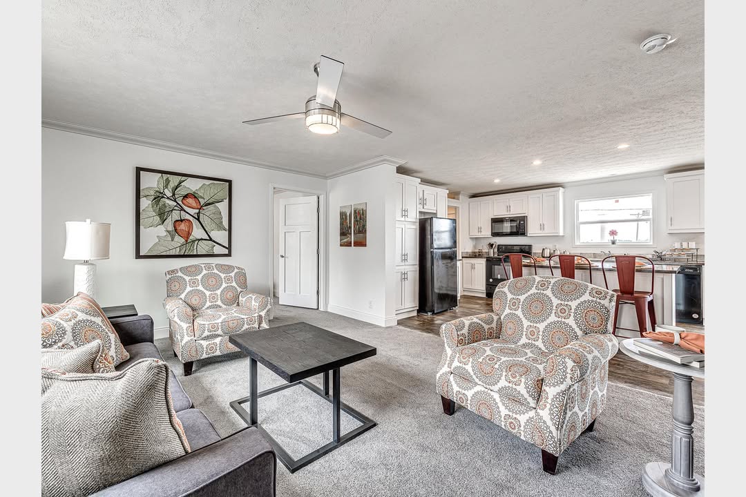 Spacious open-concept living room and kitchen with patterned armchairs, a gray sofa, and a black coffee table. Modern kitchen with bar stools and white cabinets. Cozy ambiance.
