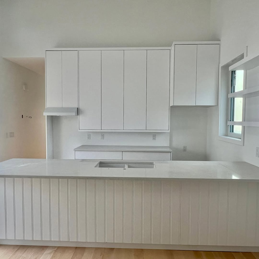 Minimalist kitchen with white cabinets and a marble countertop island. Clean lines and a bright, open feel. Light wood flooring adds warmth.