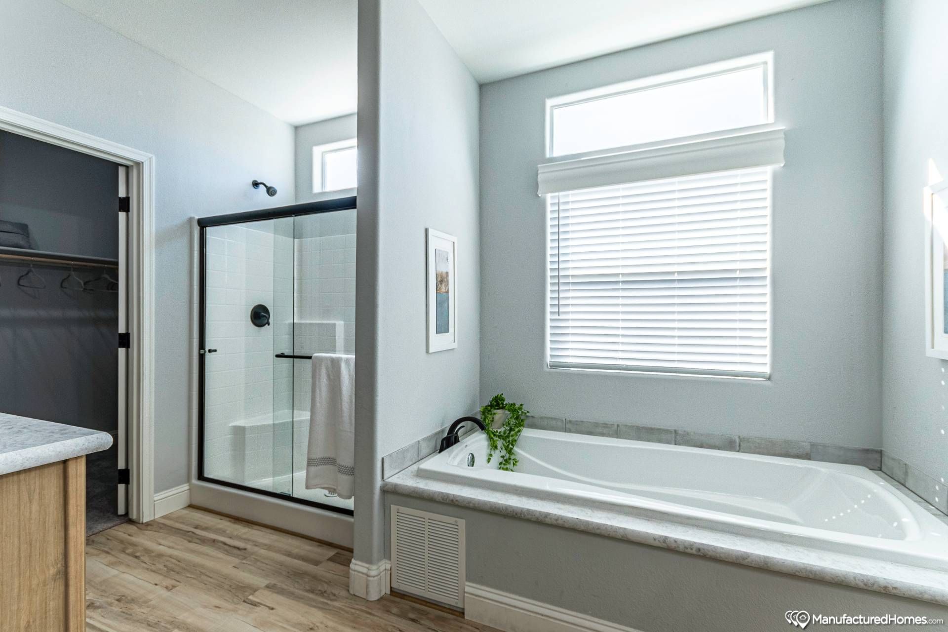 Bright modern bathroom with a large bathtub and a glass-enclosed shower. White walls, wood flooring, and potted plant create a fresh, serene atmosphere.