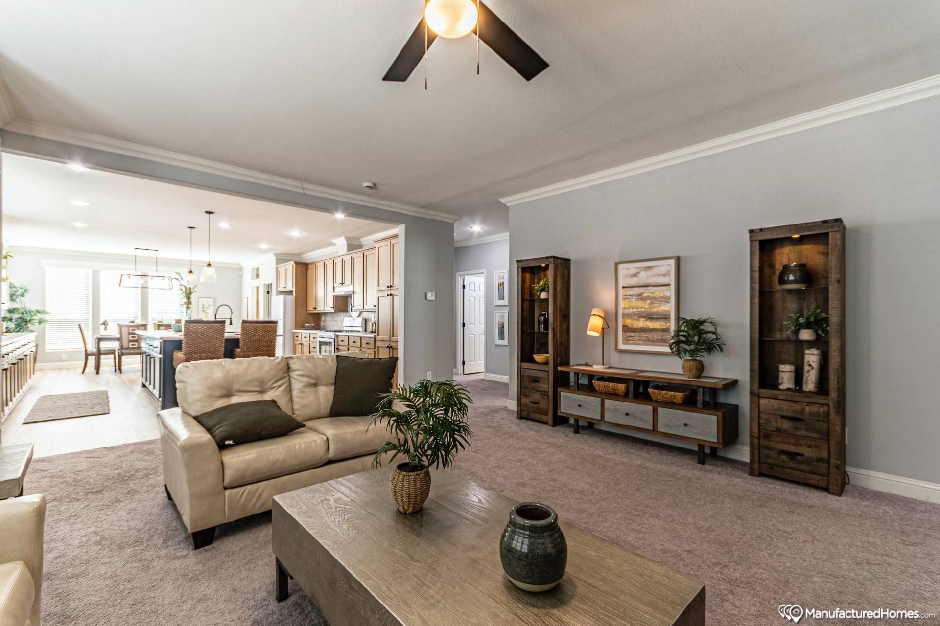 Modern living room with beige sofas, green cushions, and wooden coffee table, leading to an open kitchen. Warm lighting, neutral tones, and cozy ambiance.