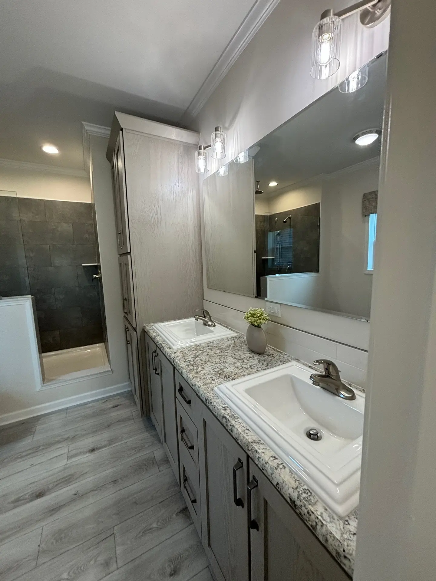 Modern bathroom with dual sinks on a granite counter, large mirror, and under-cabinet storage. Soft lighting and gray tones create a calm ambiance.