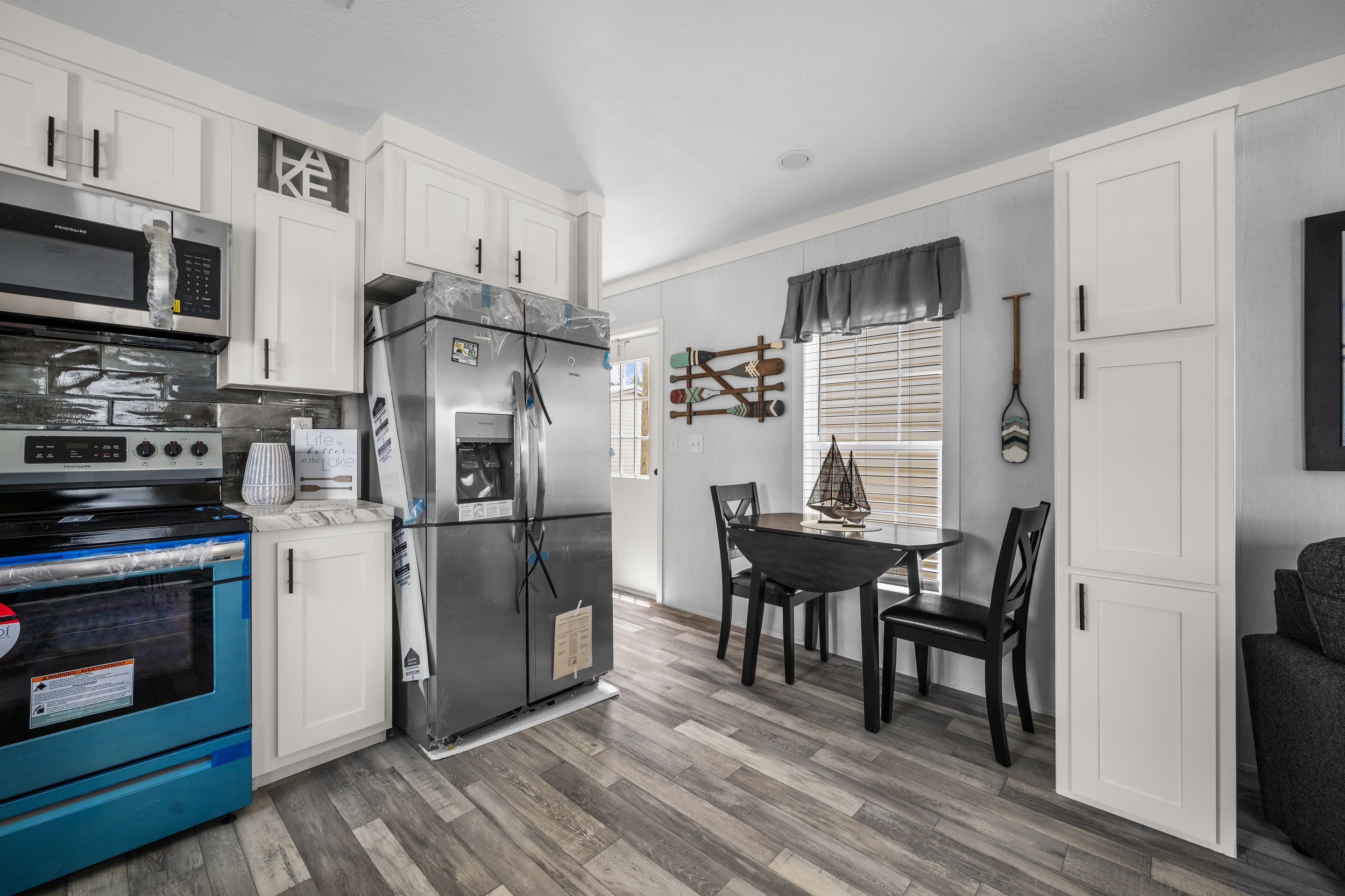 Compact, modern kitchen with white cabinets, stainless steel appliances, and wood flooring. Cozy dining area with round table, chairs, and nautical decor.