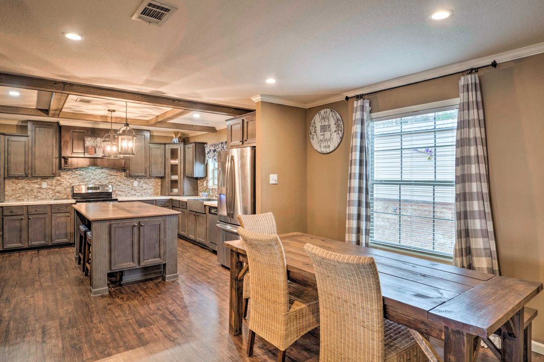 Spacious kitchen with wooden cabinets, large island, and stainless steel appliances. Adjacent dining area with a rustic table and wicker chairs. Warm, inviting tone.