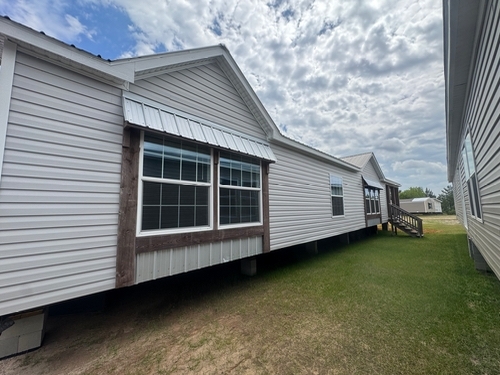 A modular home with white siding and two large windows sits on grassy terrain under a cloudy sky, conveying a sense of tranquility and modernity.