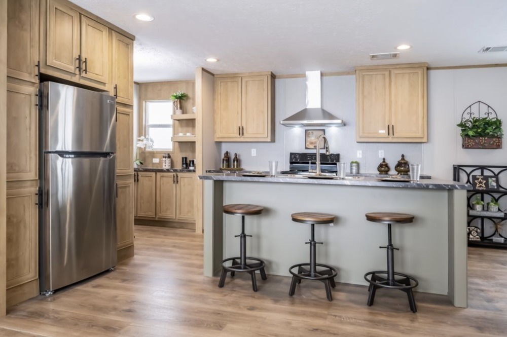 Modern kitchen with light wooden cabinets, stainless steel fridge, and a breakfast bar with three stools. The room feels bright and inviting.