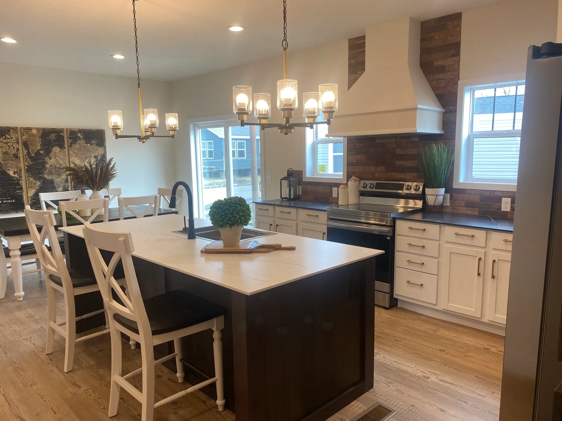 A modern kitchen with white cabinets, a brick backsplash, and a large island featuring wood accents. Elegant chandelier lighting creates a cozy atmosphere.