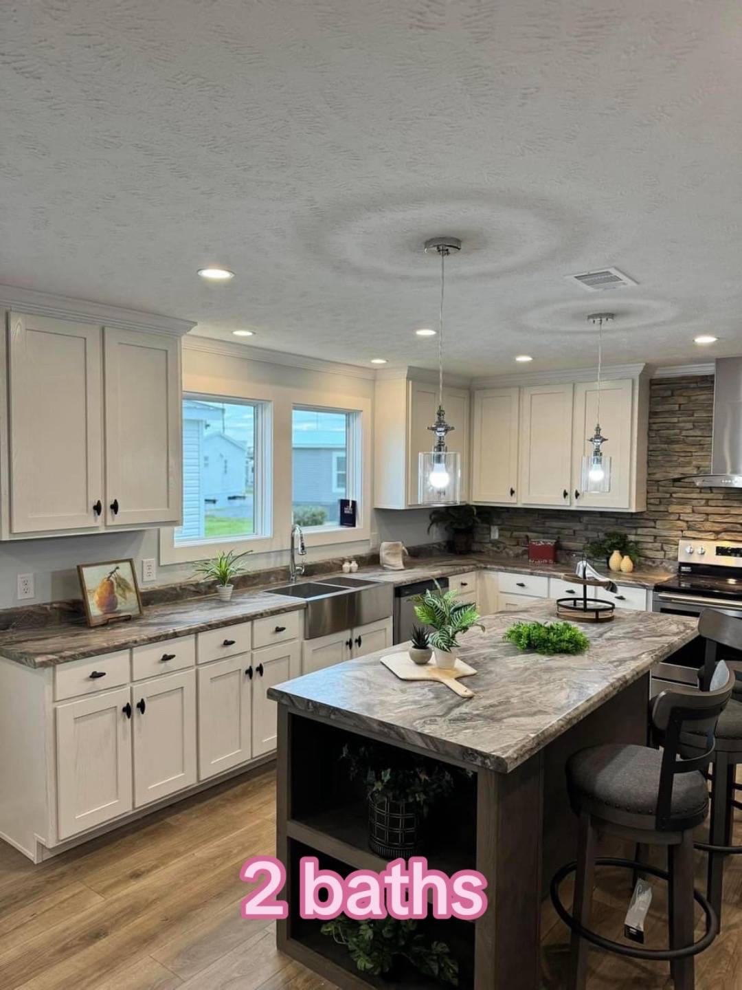 Modern kitchen featuring white cabinets, stone backsplash, and a gray marble island with bar stools. Soft lighting creates a cozy atmosphere. "2 baths" text is overlaid.