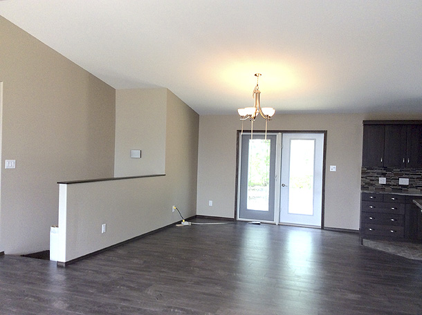 Spacious empty room with hardwood floors, beige walls, and a ceiling light fixture. French doors lead to a garden view. Modern atmosphere.