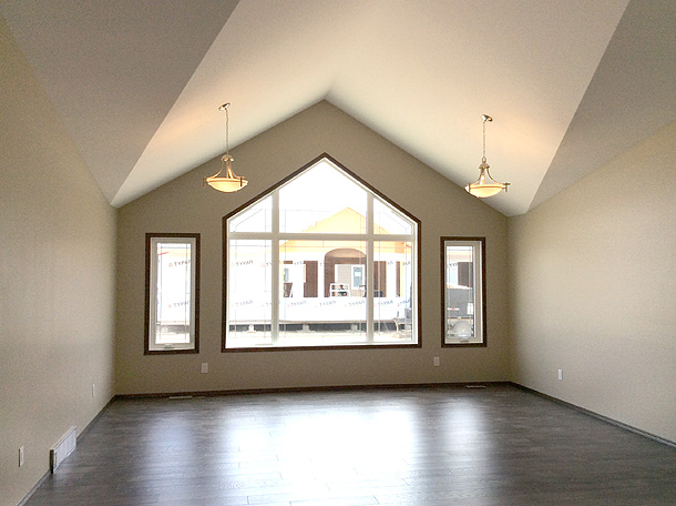 Spacious, empty room with vaulted ceiling, large triangular window, and two pendant lights. Natural light creates an airy, minimalist atmosphere.