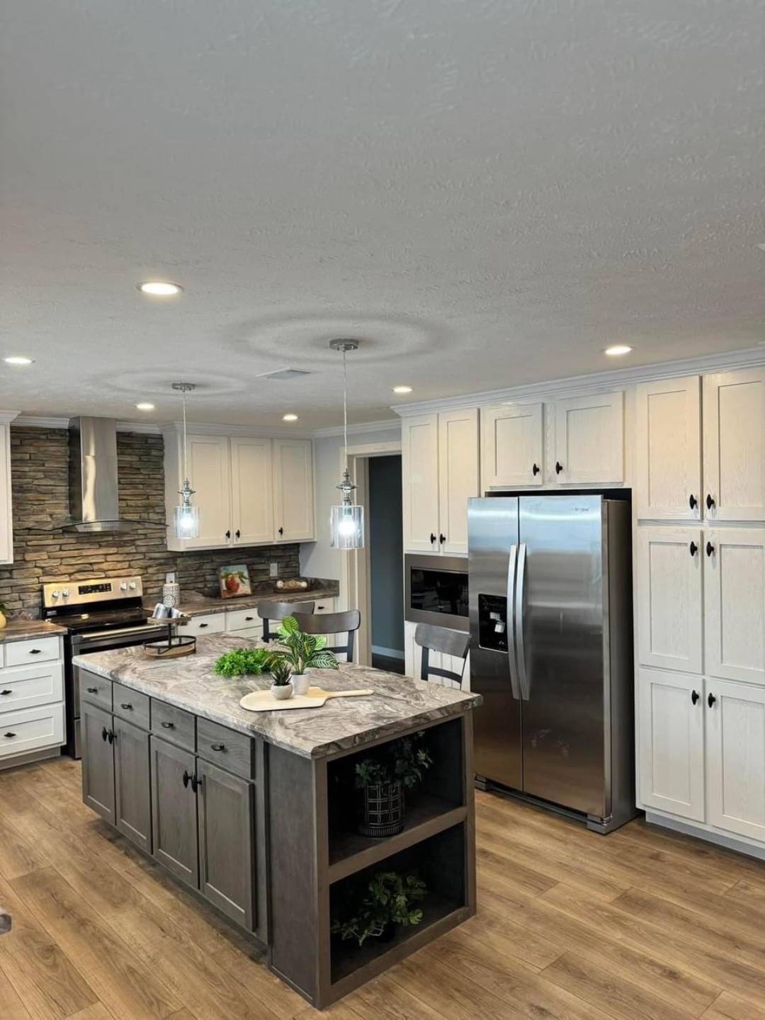 Modern kitchen with a stone backsplash, stainless steel appliances, and white cabinets. Central island features a marble countertop and pendant lighting.