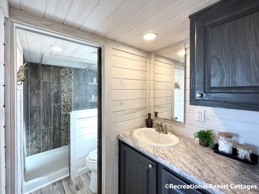 Small modern bathroom with rustic wood paneling. Features include a granite countertop, under-mount sink, sleek fixtures, and a tiled shower with a glass door.