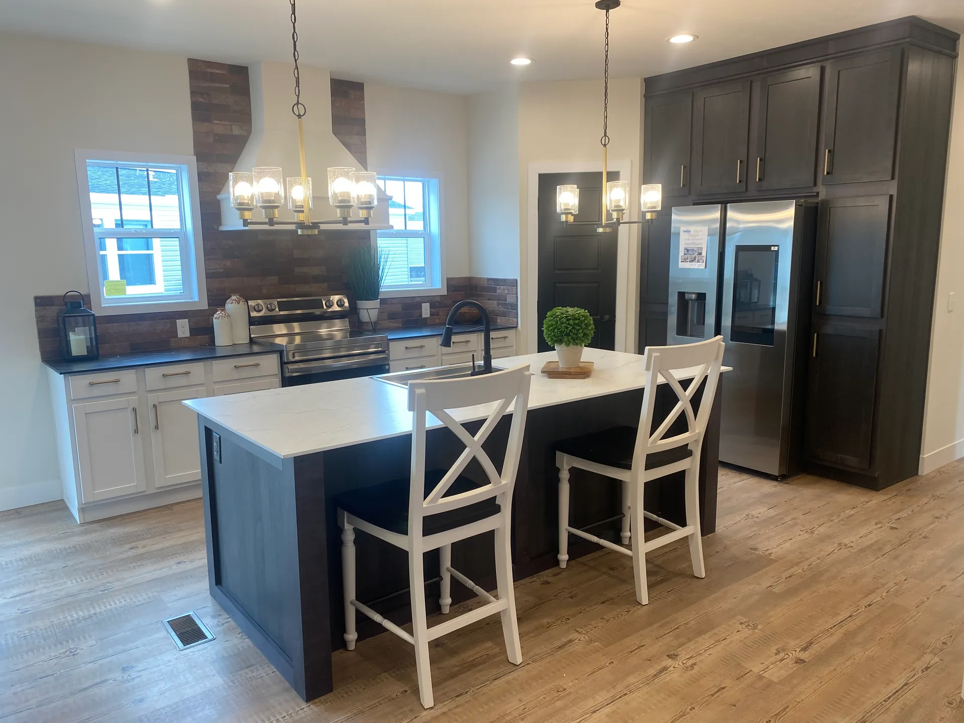 Modern kitchen with dark wood cabinets, a white island, and two white chairs. Stainless steel appliances and warm lighting create a cozy atmosphere.
