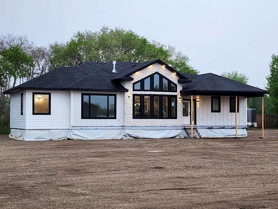 Single-story, white modern house with black-trimmed windows under a cloudy sky. Surrounded by trees, the exterior is covered in protective tarp.
