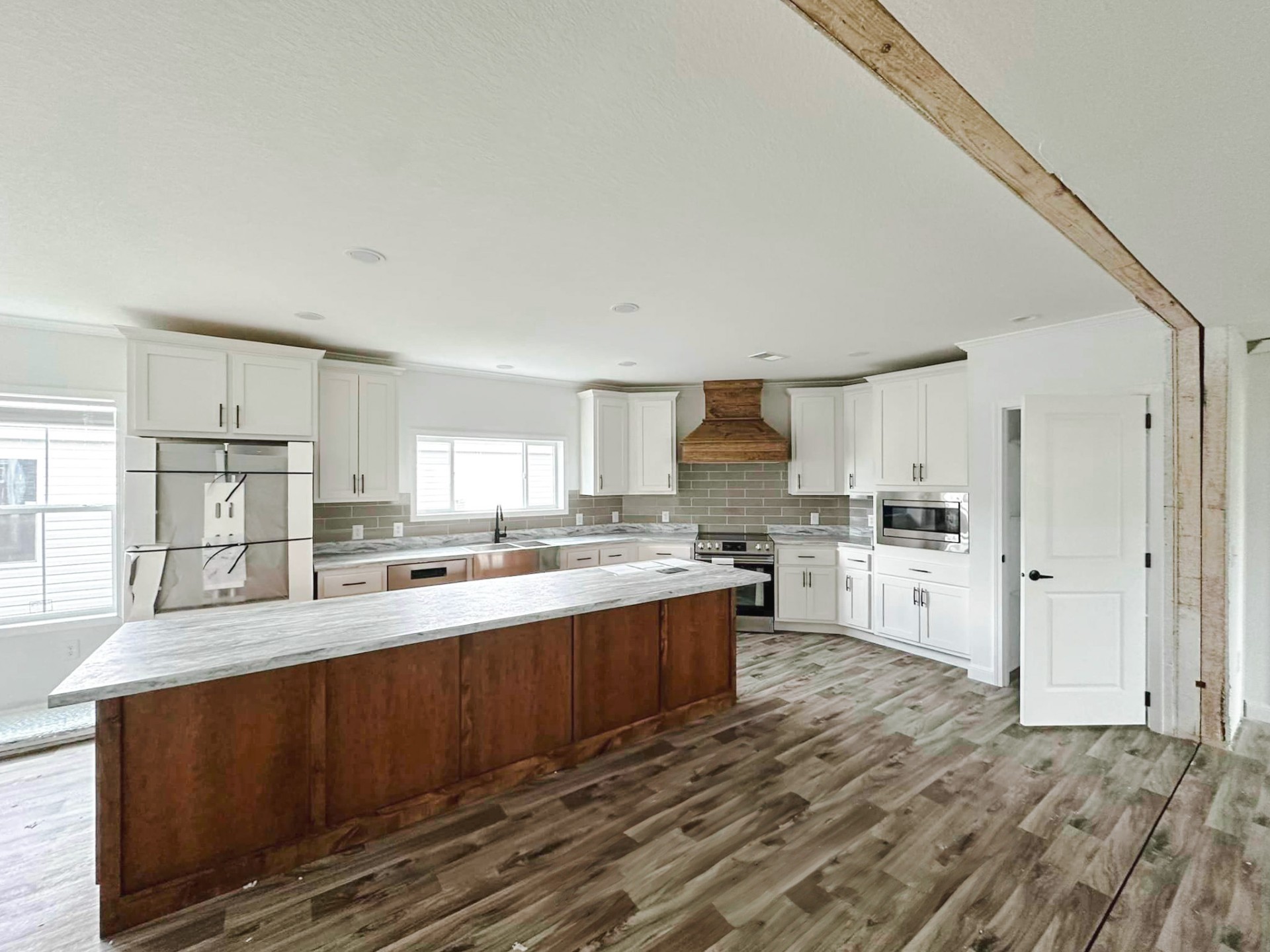 Spacious modern kitchen with a large wooden island, white cabinets, stainless steel appliances, and gray backsplash. Bright with natural light, cozy ambiance.