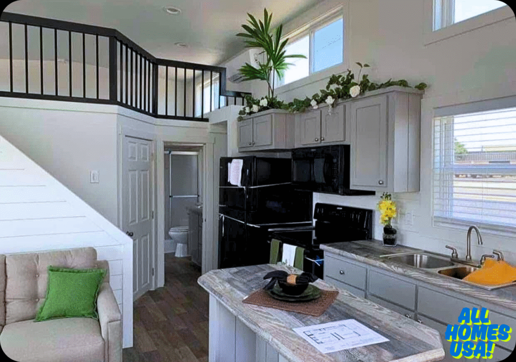 Modern tiny home kitchen with gray cabinets, black appliances, and a cozy loft area. Bright, airy space with plants and natural light filtering in. Image for illustrative purposes.