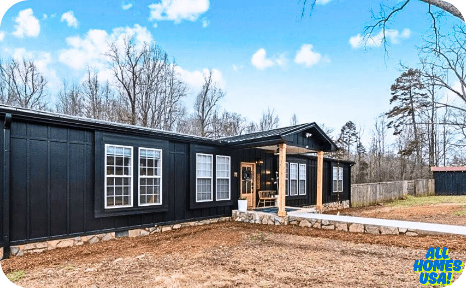 Exterior of a modern black house with large windows, a front porch, and a stone walkway, set in a wooded landscape under a blue sky. Image for illustrative purpose.
