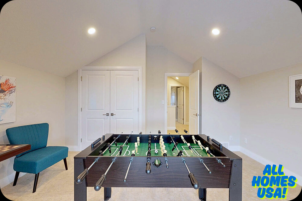 Room with sloped ceilings features foosball table and dartboard. A turquoise chair and abstract wall art add color. Bright and playful atmosphere. Image for illustrative purpose.