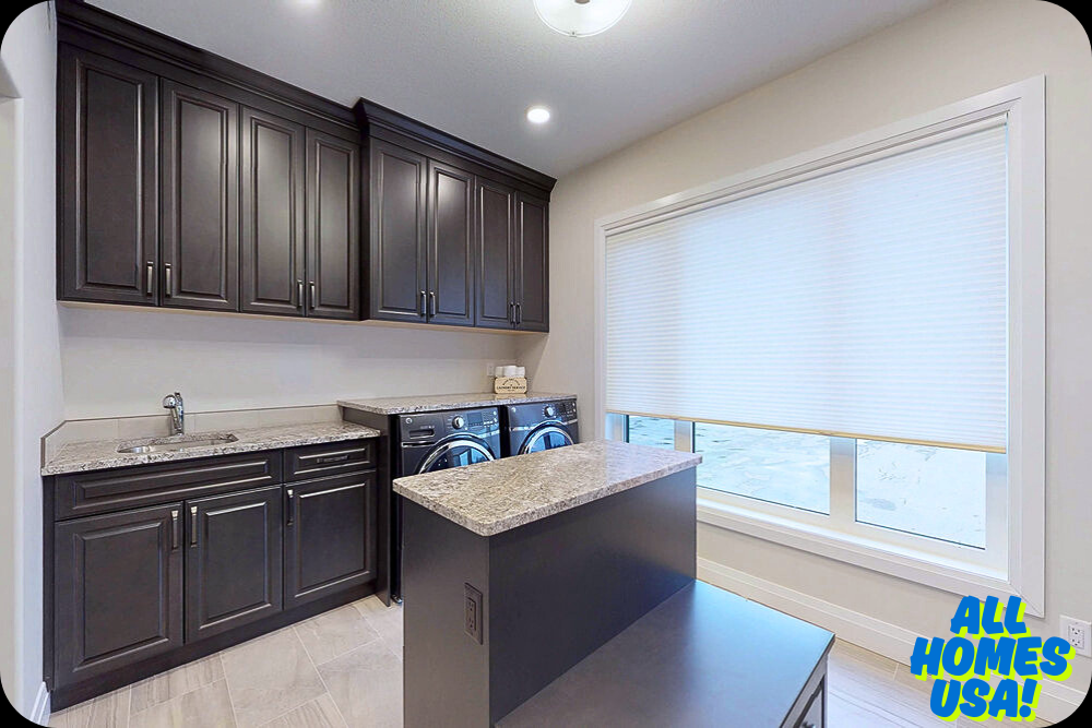 Modern laundry room with dark brown cabinets, granite countertops, and stainless steel sink. Front-loading washer and dryer beneath cupboards. Large window with blinds. Bright and clean atmosphere. Logo reads "All Homes USA!" in the corner.