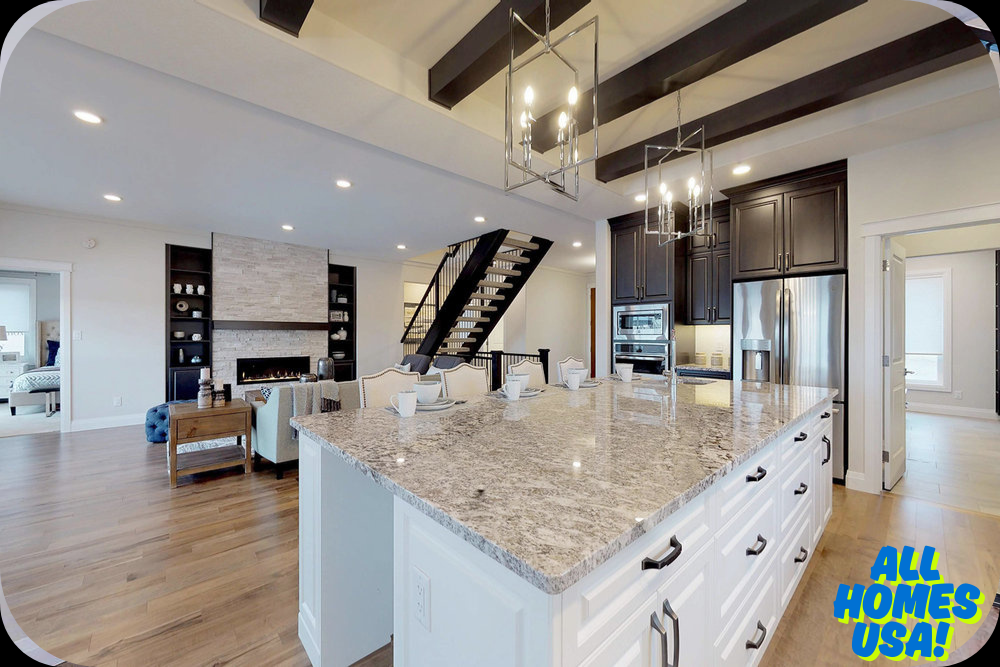 Modern kitchen and living area with a large granite island, elegant chandeliers, dark wood cabinets, a cozy seating area, and a staircase. Warm, inviting tone. Image for illustrative purpose.