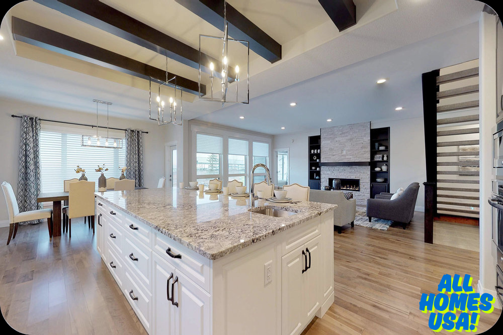 Spacious modern kitchen and living area with a large granite island, white cabinets, and dark ceiling beams. Cozy seating near a stone fireplace. Image for illustrative purpose.