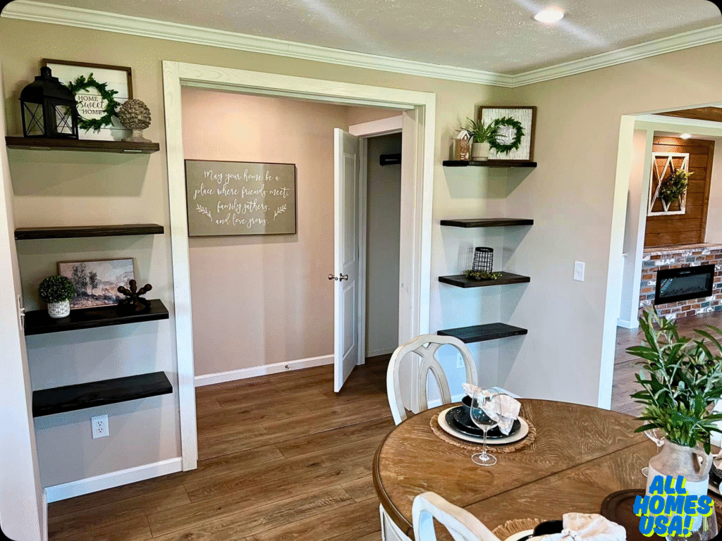 Cozy dining area with beige walls, wood floors, and a round table set for two. Shelves with decor frames surround a sign with an inviting message. Image for illustrative purposes.