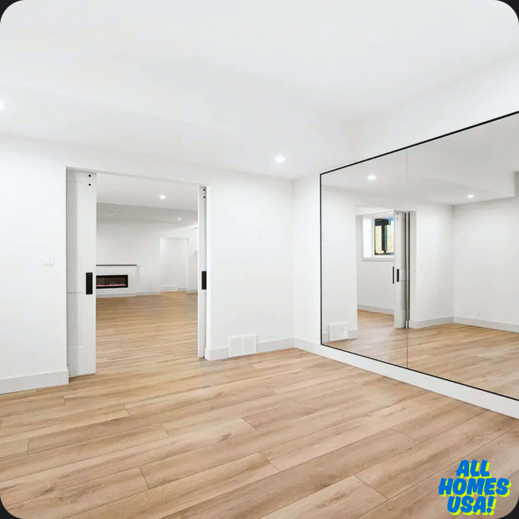 Spacious, empty room with wooden floors, white walls, and large mirrors. Sliding doors open to another area. Bright, modern, and minimalistic design. Image for illustrative purpose.