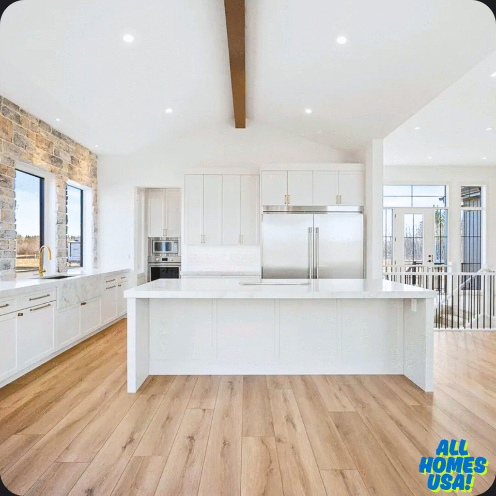 Spacious modern kitchen with white cabinets, marble countertops, and stainless steel appliances. Stone accent wall and large windows provide natural light. Image for illustrative purpose.