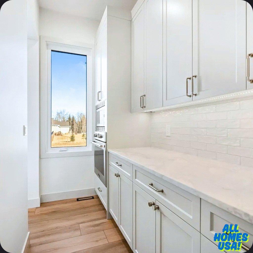 Bright, minimalist kitchen with white cabinets and countertops, wooden floor, vertical window showing a clear sky and trees outside, evoking a fresh, airy feel. Image for illustrative purpose.
