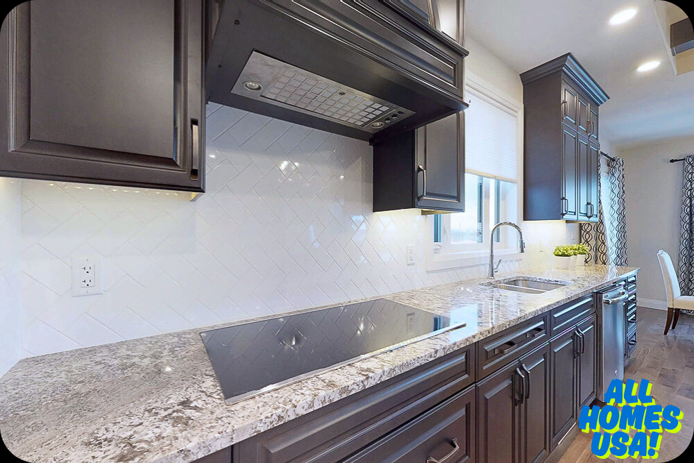 Modern kitchen with dark cabinets, white herringbone tile backsplash, and granite countertops. Bright, clean ambiance with built-in stovetop and sink. Image for illustrative purpose.