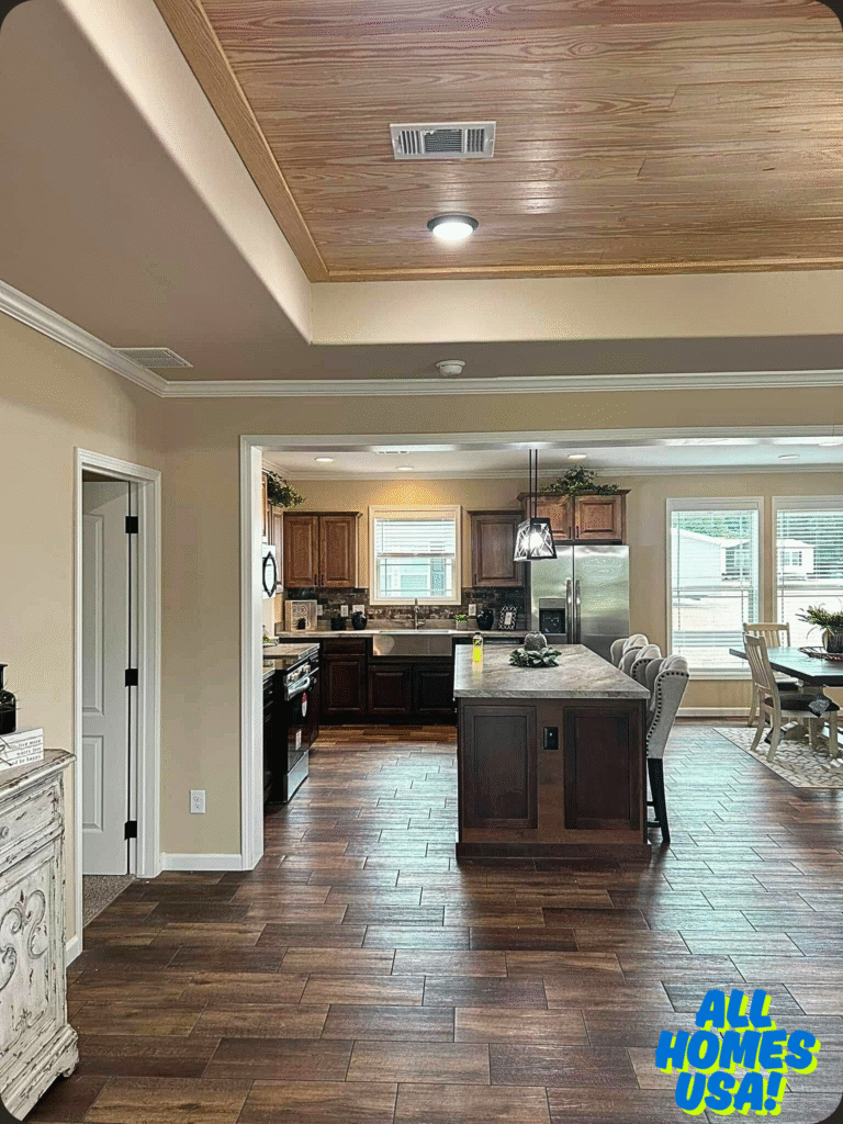 Spacious kitchen with dark wood cabinets, central island, and tile flooring. Dining area with upholstered chairs visible. Text "All Homes USA!" in corner. Image for illustrative purpose.