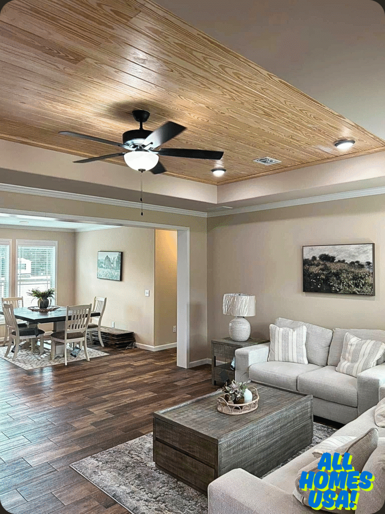Living room with a light wood ceiling, dark wood floors, and a modern ceiling fan. Beige couch, gray table, and dining area create a cozy, inviting space. Image for illustrative purpose.