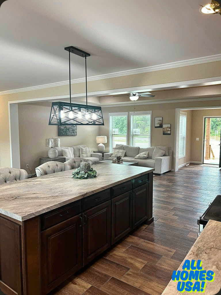 Spacious kitchen with dark wood island, marble countertop, modern pendant light. Cozy living area with beige couches, large windows, and warm wood flooring. Image for illustrative purpose.