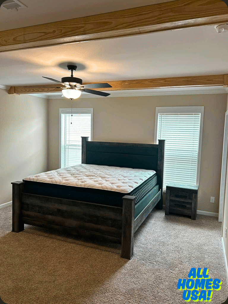 Spacious bedroom with a dark wooden bed and white mattress. Carpeted floor, two large windows, and a ceiling fan. Calm, minimalist vibe. Image for illustrative purpose.