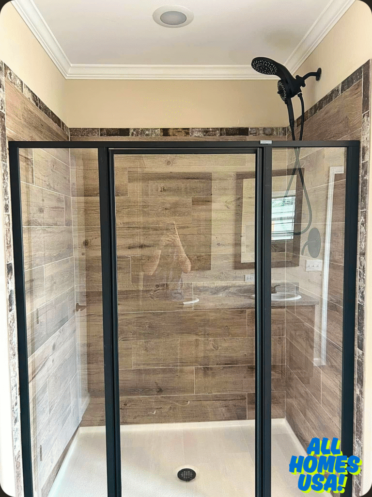 Enclosed shower with glass doors, wood-patterned tile walls, and a black rain showerhead. Bright, modern bathroom design conveys elegance. Image for illustrative purpose.