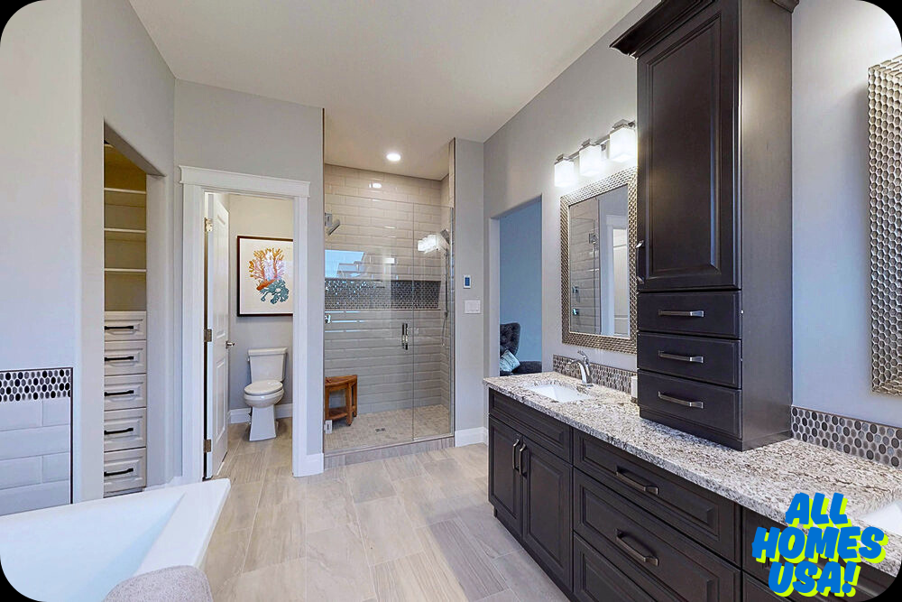 Spacious, modern bathroom with light gray walls and tile flooring. Features a glass-enclosed shower, dark wood vanity with granite countertop, and bright lighting. Image for illustrative purpose.