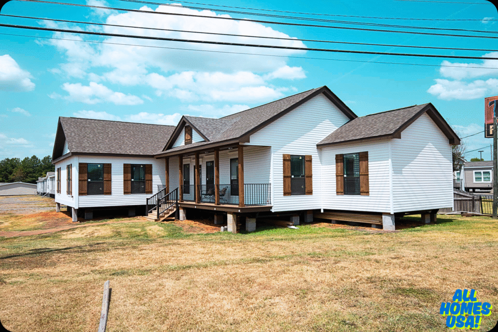 A white manufactured home on a grassy lot under a bright blue sky. It features brown shutters, a porch with black railings, and a shingled roof. Image for illustrative purpose.