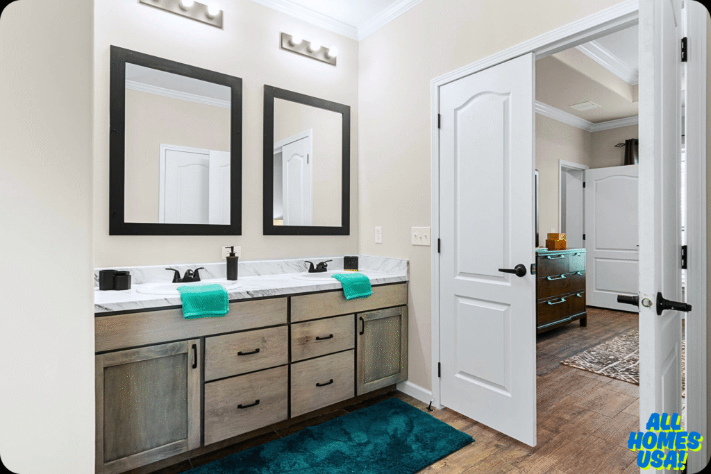 Modern bathroom with double sinks, teal towels, and a teal rug on wooden flooring. Two large mirrors and bright lighting create a fresh, clean vibe. Image for illustrative purpose.