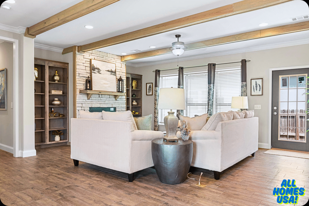 Bright, cozy living room with beige sectional, gray wooden side table, modern decor, wood beams, stone fireplace, and large windows with curtains. Image for illustrative purpose.